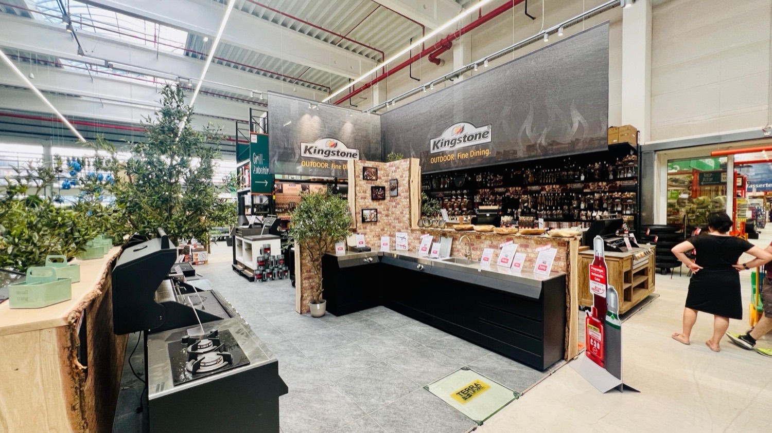 Bauhaus Stadtgarten: the Kingstone grill and outdoor cooking department with dark counters and olive trees
