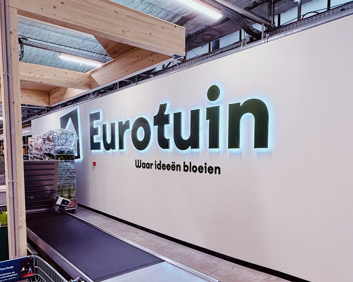 Eurotuin Merelbeke: backlit Eurotuin logo wall with the tagline 'Waar ideeën bloeien' above the checkout belt